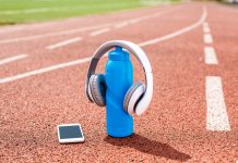 Headphones placed on a blue water bottle with a smartphone on a running track, illustrating the integration of music into athletic training routines.