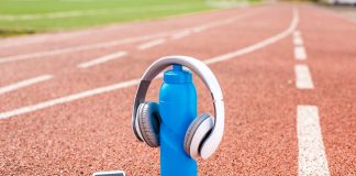 Headphones placed on a blue water bottle with a smartphone on a running track, illustrating the integration of music into athletic training routines.