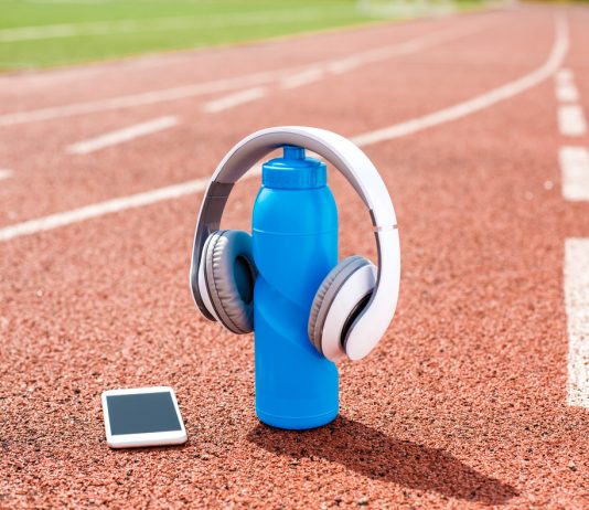 Training Tunes: Training Tunes: Boosting Athletic Performance with Music at the 2024 Olympics Headphones placed on a blue water bottle with a smartphone on a running track, illustrating the integration of music into athletic training routines.